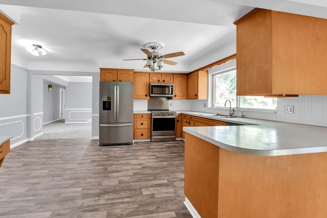 kitchen featuring sink, light hardwood / wood-style flooring, kitchen peninsula, stainless steel appliances, and backsplash