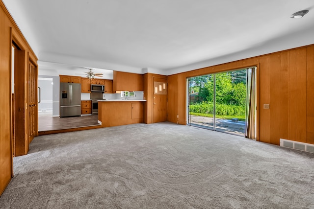 unfurnished living room featuring light carpet, ceiling fan, and wood walls