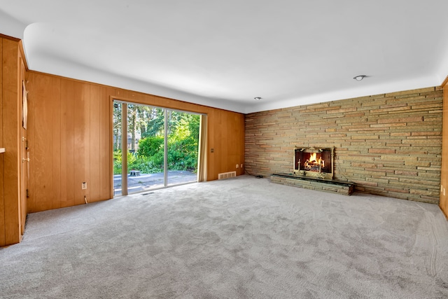 unfurnished living room featuring a fireplace, wooden walls, and carpet flooring