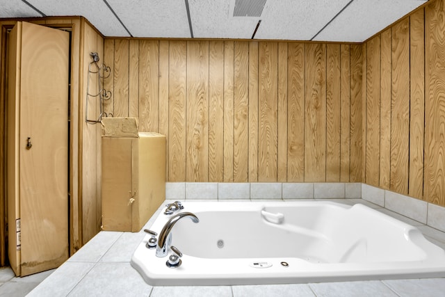 bathroom featuring tiled tub, a drop ceiling, and wood walls