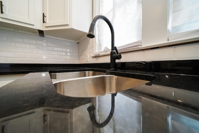 interior details with white cabinetry, sink, backsplash, and dark stone countertops