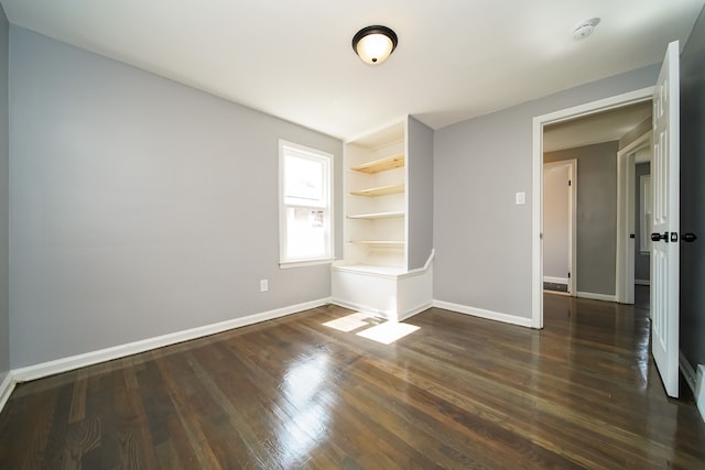 spare room with built in shelves and dark hardwood / wood-style floors