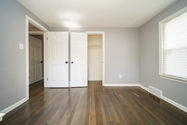 unfurnished bedroom featuring dark wood-type flooring, a closet, and multiple windows