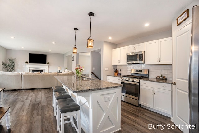 kitchen with white cabinetry, stainless steel appliances, an island with sink, a kitchen bar, and dark stone counters