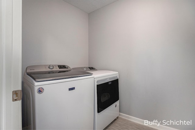 clothes washing area with washing machine and clothes dryer, a textured ceiling, and light hardwood / wood-style floors