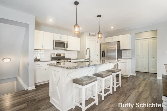 kitchen featuring stainless steel appliances, an island with sink, sink, and white cabinetry