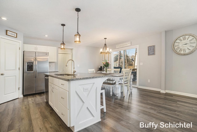 kitchen with an island with sink, white cabinetry, sink, dark stone counters, and stainless steel appliances