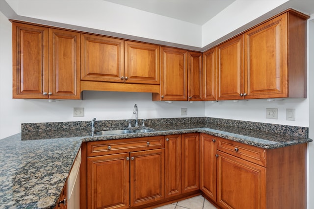 kitchen with dark stone countertops, brown cabinets, light tile patterned floors, and a sink