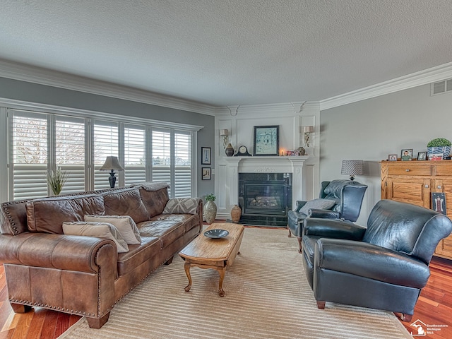 living room with a tiled fireplace, ornamental molding, a textured ceiling, and light hardwood / wood-style floors