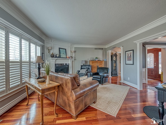 living room with hardwood / wood-style floors, crown molding, a textured ceiling, and ornate columns