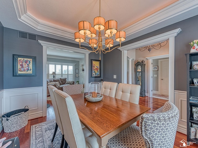 dining area featuring a raised ceiling, ornamental molding, hardwood / wood-style flooring, and a chandelier