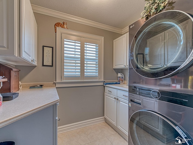 laundry area featuring stacked washer and clothes dryer, cabinets, a textured ceiling, light tile patterned floors, and ornamental molding