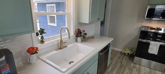 kitchen with sink, light hardwood / wood-style floors, green cabinetry, and appliances with stainless steel finishes