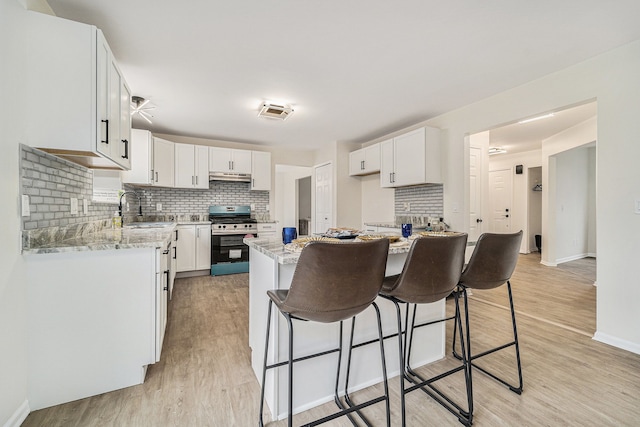 kitchen with sink, stainless steel gas range, light stone countertops, white cabinets, and light wood-type flooring