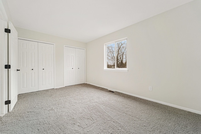 unfurnished bedroom with two closets and carpet floors