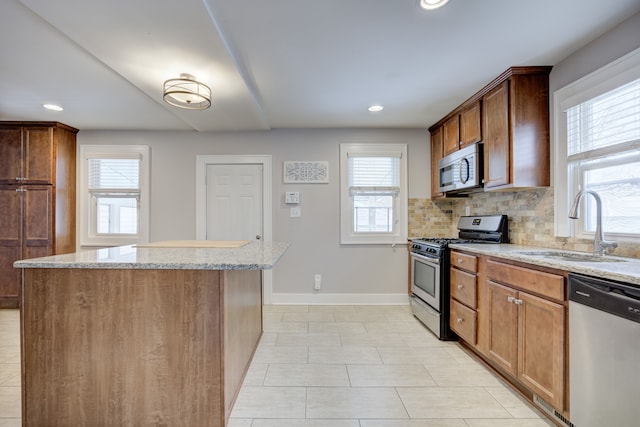 kitchen with light stone counters, stainless steel appliances, sink, and a kitchen island