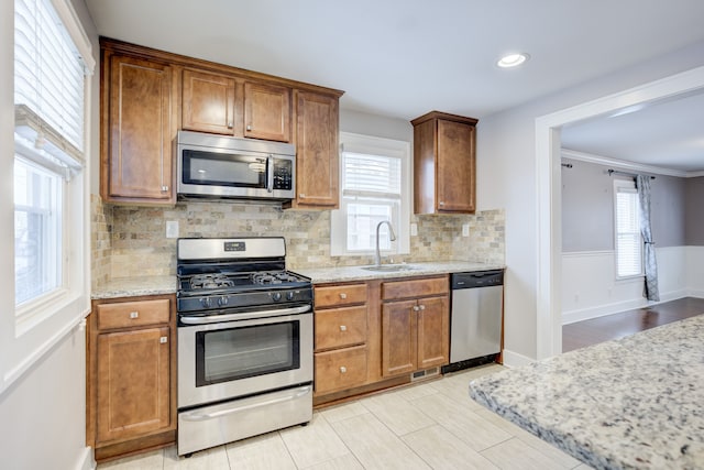 kitchen with stainless steel appliances, a healthy amount of sunlight, sink, and light stone counters