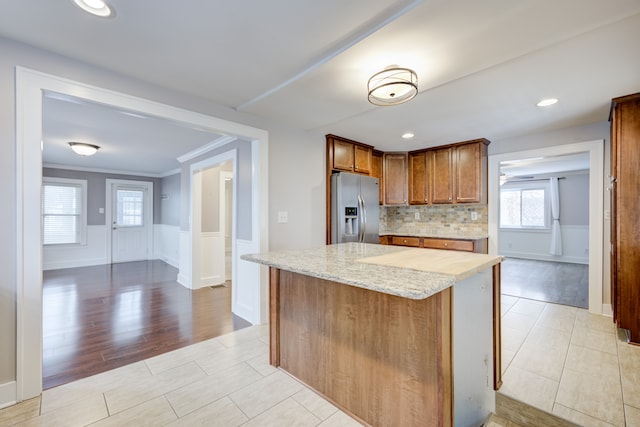 kitchen with light stone counters, tasteful backsplash, ornamental molding, stainless steel fridge, and a kitchen island