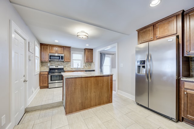 kitchen with sink, appliances with stainless steel finishes, a center island, tasteful backsplash, and light stone countertops