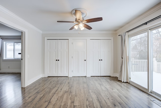 unfurnished bedroom with crown molding, access to outside, light hardwood / wood-style floors, and two closets