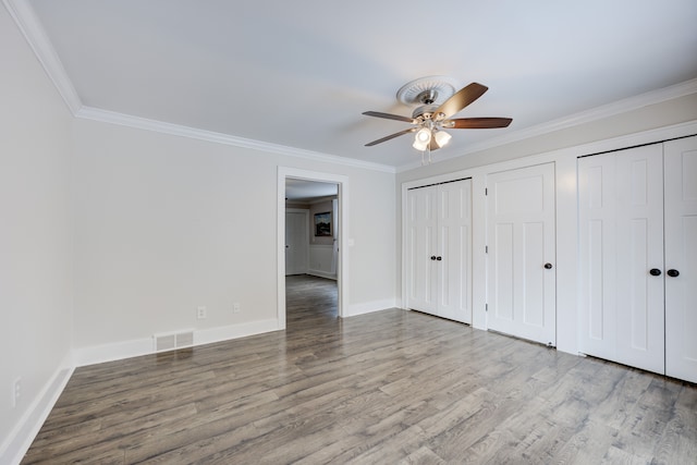 unfurnished bedroom with wood-type flooring, two closets, ceiling fan, and crown molding