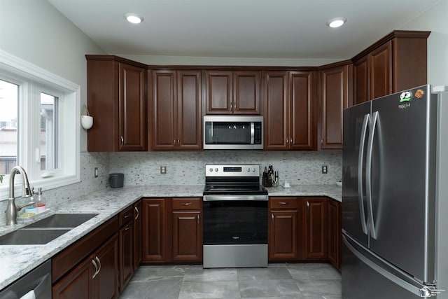 kitchen featuring sink, stainless steel appliances, dark brown cabinetry, light stone countertops, and decorative backsplash