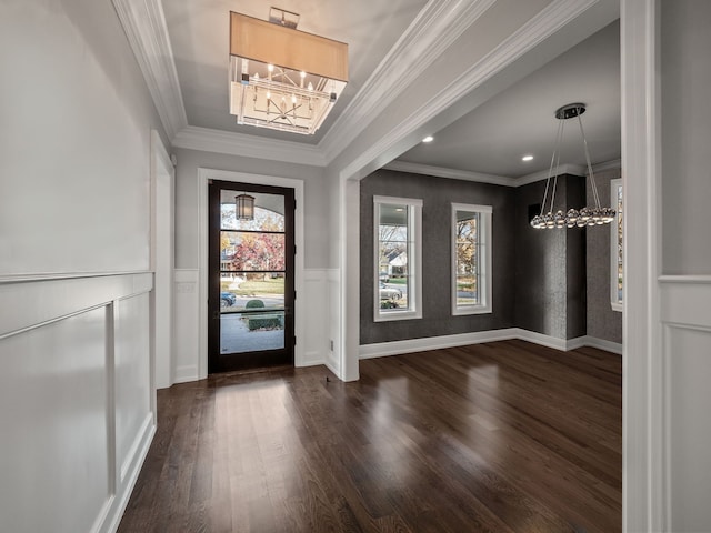 entrance foyer featuring dark wood-style flooring, a notable chandelier, ornamental molding, wainscoting, and baseboards