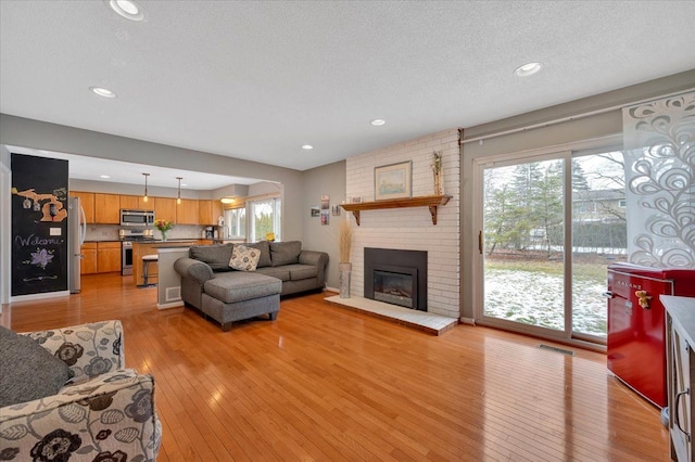 living room featuring a brick fireplace, a wealth of natural light, a textured ceiling, and light wood-type flooring