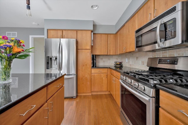 kitchen featuring backsplash, stainless steel appliances, light hardwood / wood-style flooring, and dark stone countertops