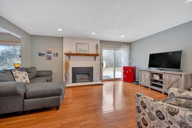 living room with a textured ceiling, a wealth of natural light, a fireplace, and light hardwood / wood-style floors