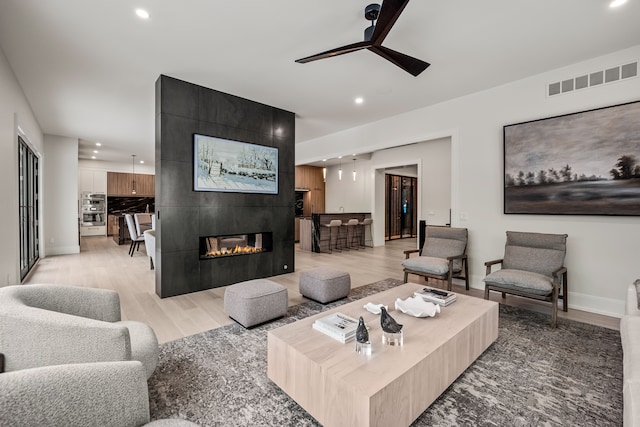 living room with a tiled fireplace, light hardwood / wood-style flooring, and ceiling fan