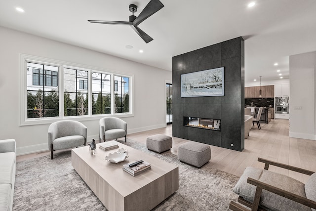 living room with ceiling fan, light wood-type flooring, and a fireplace