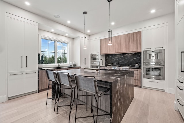 kitchen featuring a kitchen island with sink, sink, white cabinets, and decorative light fixtures