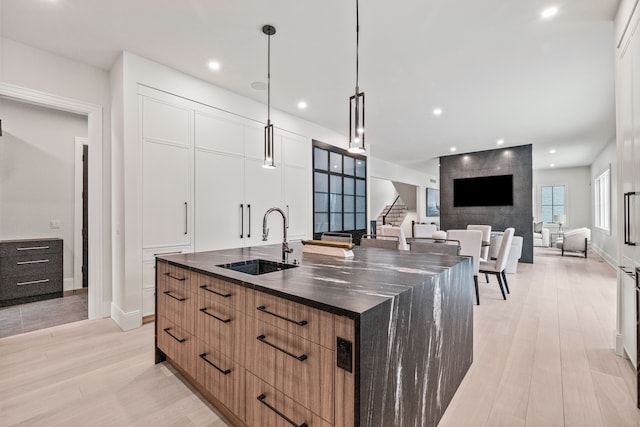 kitchen featuring pendant lighting, sink, light hardwood / wood-style flooring, white cabinetry, and a large island with sink