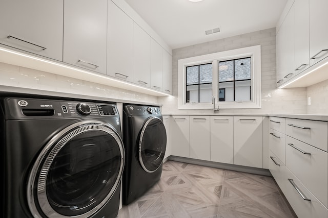 laundry area with cabinets, light parquet flooring, and washer and dryer