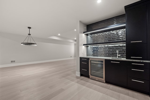 bar with decorative light fixtures, sink, beverage cooler, backsplash, and light wood-type flooring