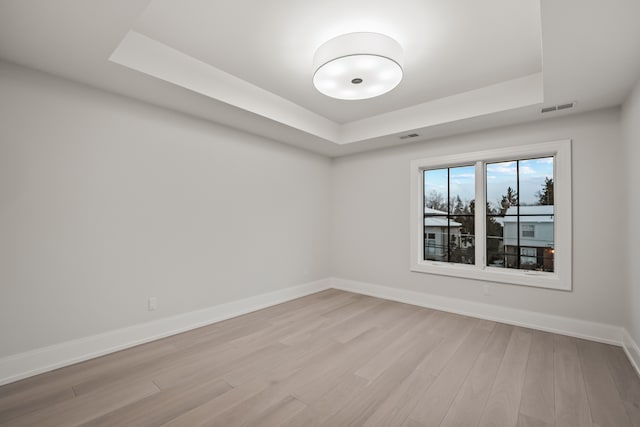 spare room with a tray ceiling and light hardwood / wood-style floors