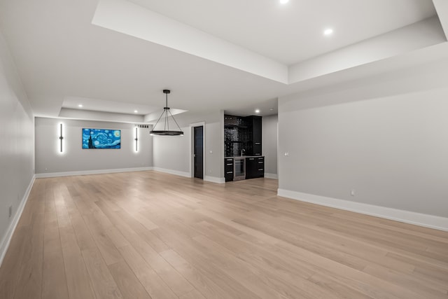 unfurnished living room with bar, a raised ceiling, and light hardwood / wood-style floors