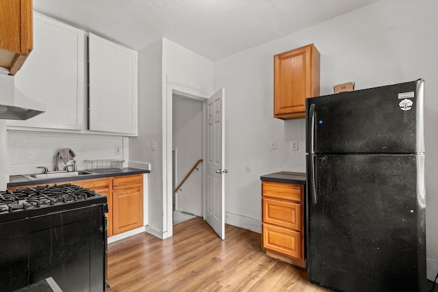 kitchen with sink, black appliances, a textured ceiling, light wood-type flooring, and wall chimney range hood