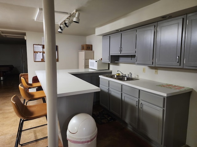 kitchen with a kitchen breakfast bar, kitchen peninsula, sink, and gray cabinetry