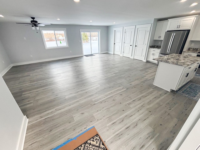 kitchen featuring stainless steel fridge, white cabinets, hardwood / wood-style flooring, ceiling fan, and light stone counters