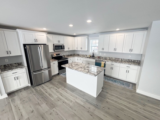 kitchen with sink, white cabinetry, appliances with stainless steel finishes, a kitchen island, and light stone countertops