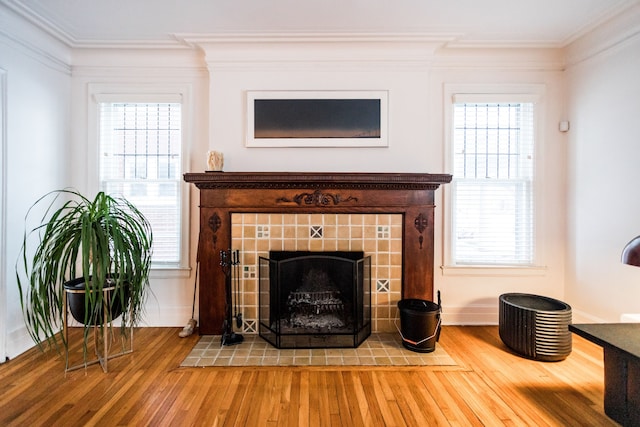 living area featuring ornamental molding, plenty of natural light, a tile fireplace, and wood-type flooring