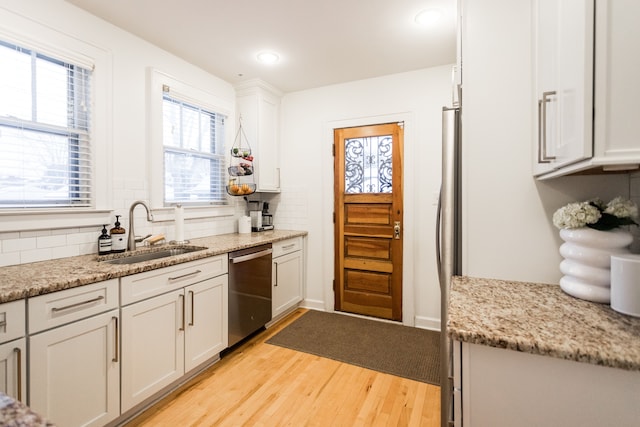 kitchen featuring light stone counters, sink, stainless steel dishwasher, and white cabinets