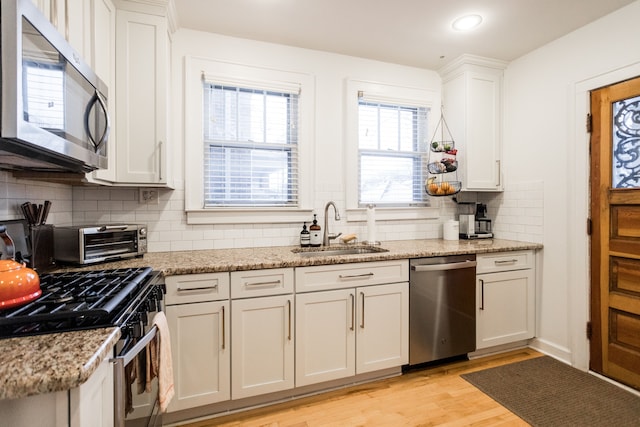 kitchen with sink, white cabinetry, stainless steel appliances, light stone countertops, and light wood-type flooring