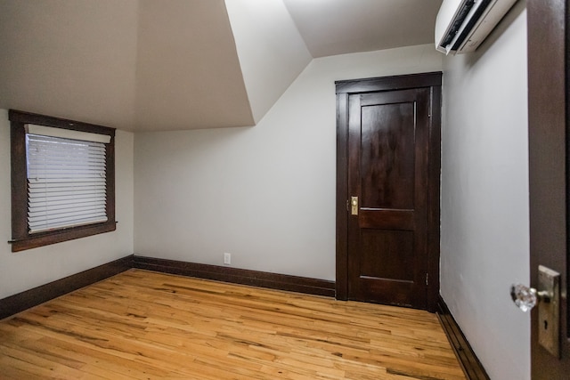 additional living space featuring lofted ceiling, a wall mounted air conditioner, and light wood-type flooring