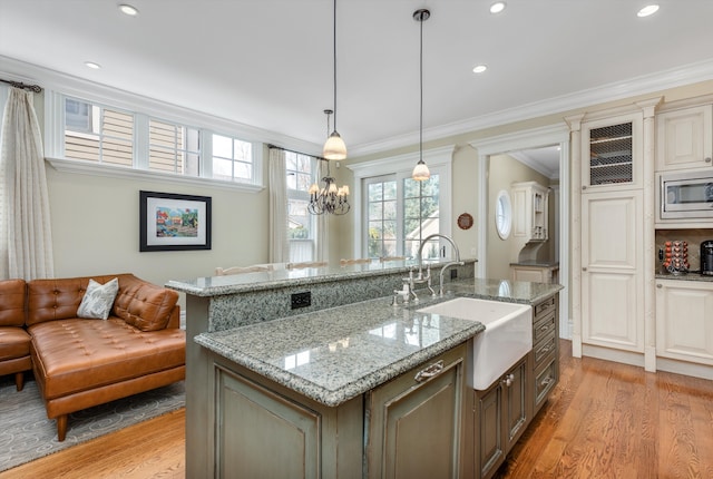 kitchen featuring stainless steel microwave, decorative light fixtures, an island with sink, sink, and ornamental molding