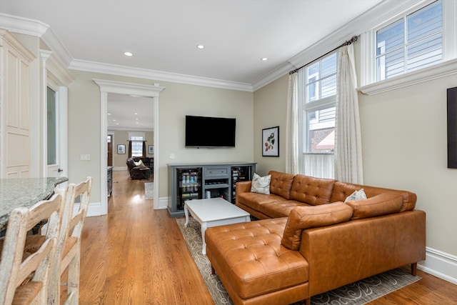 living room with ornamental molding, beverage cooler, and light hardwood / wood-style flooring