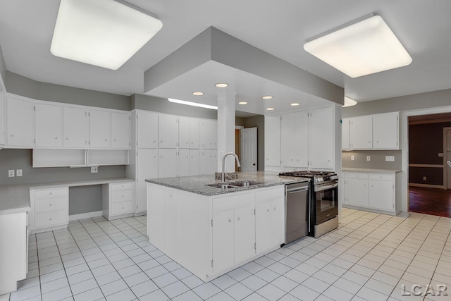 kitchen with built in desk, sink, white cabinets, stainless steel appliances, and a center island with sink