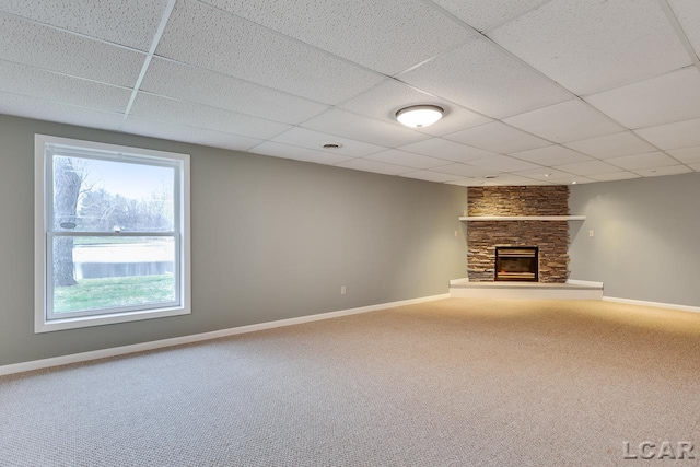 unfurnished living room featuring a stone fireplace, carpet floors, and a drop ceiling